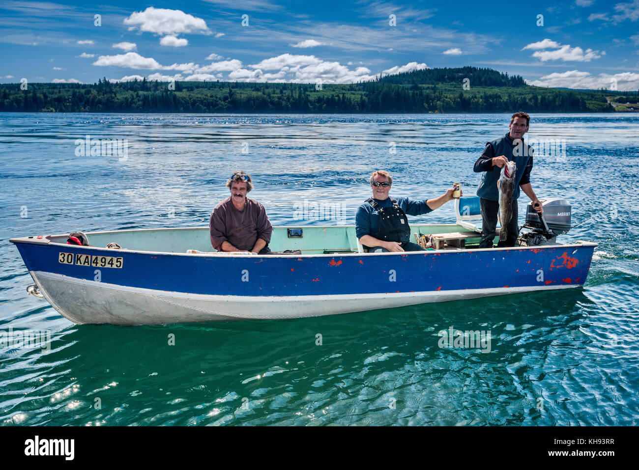 Tres hombres que muestran pescado que capturaron, salmón, en un pequeño barco, en el estrecho de Johnstone, en la isla de Vancouver, Columbia Británica, Canadá Foto de stock