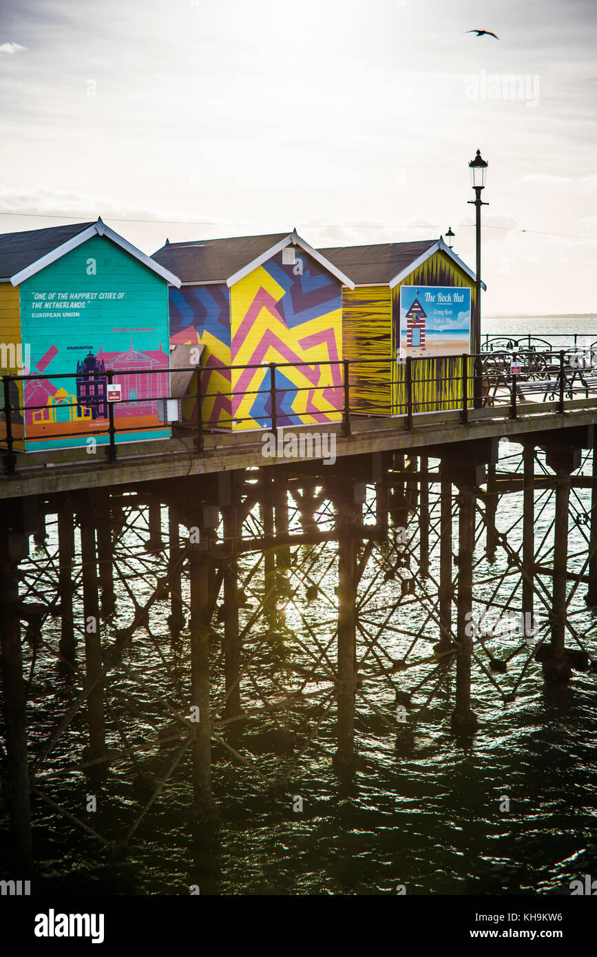 Cabañas de colores brillantes en el extremo de Southend Pier con estructura de celosía de patas de hierro mirando hacia el sol y el estuario del Támesis, Essex, Reino Unido Foto de stock