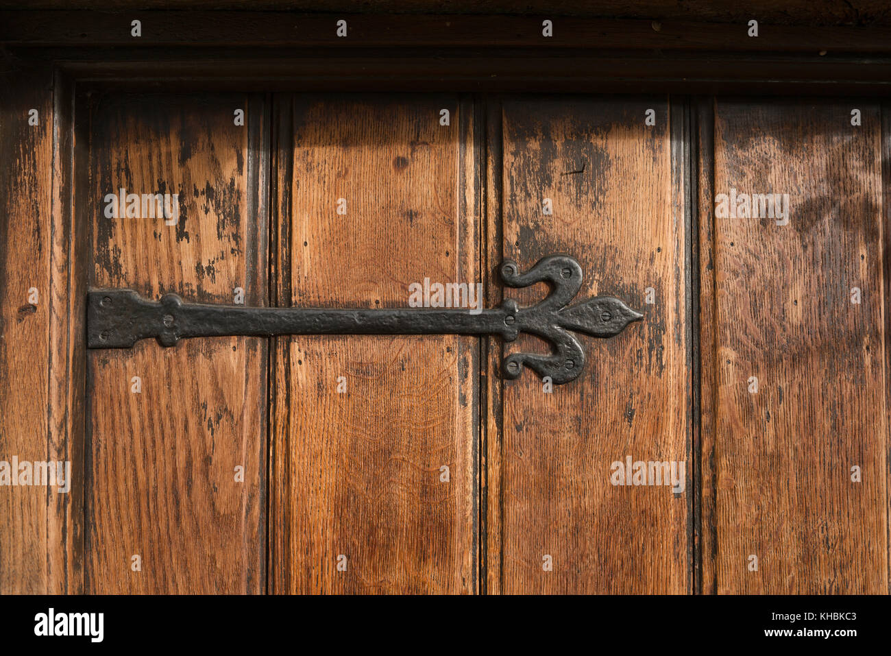 Un sustancial de hierro fundido negro, ornamentado, bisagra de antigüedades montado en un anciano, de lengüeta y ranura de la puerta delantera del roble. Foto de stock
