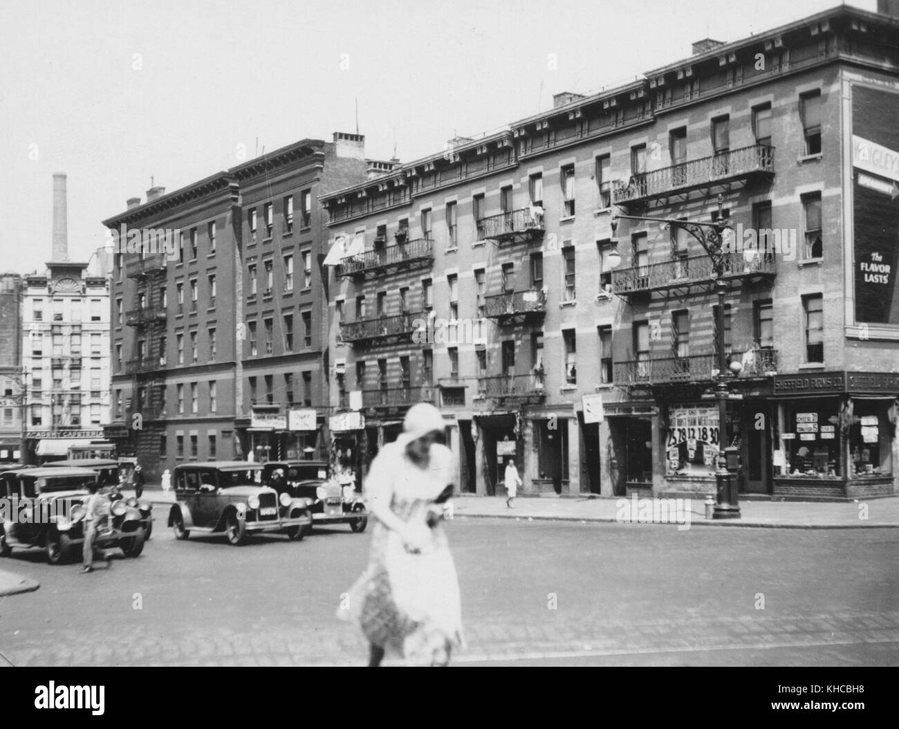 Mujer en un vestido blanco prisas en un cruce, coches visible esperando en el segundo plano, 1920. A partir de la biblioteca pública de Nueva York. Foto de stock