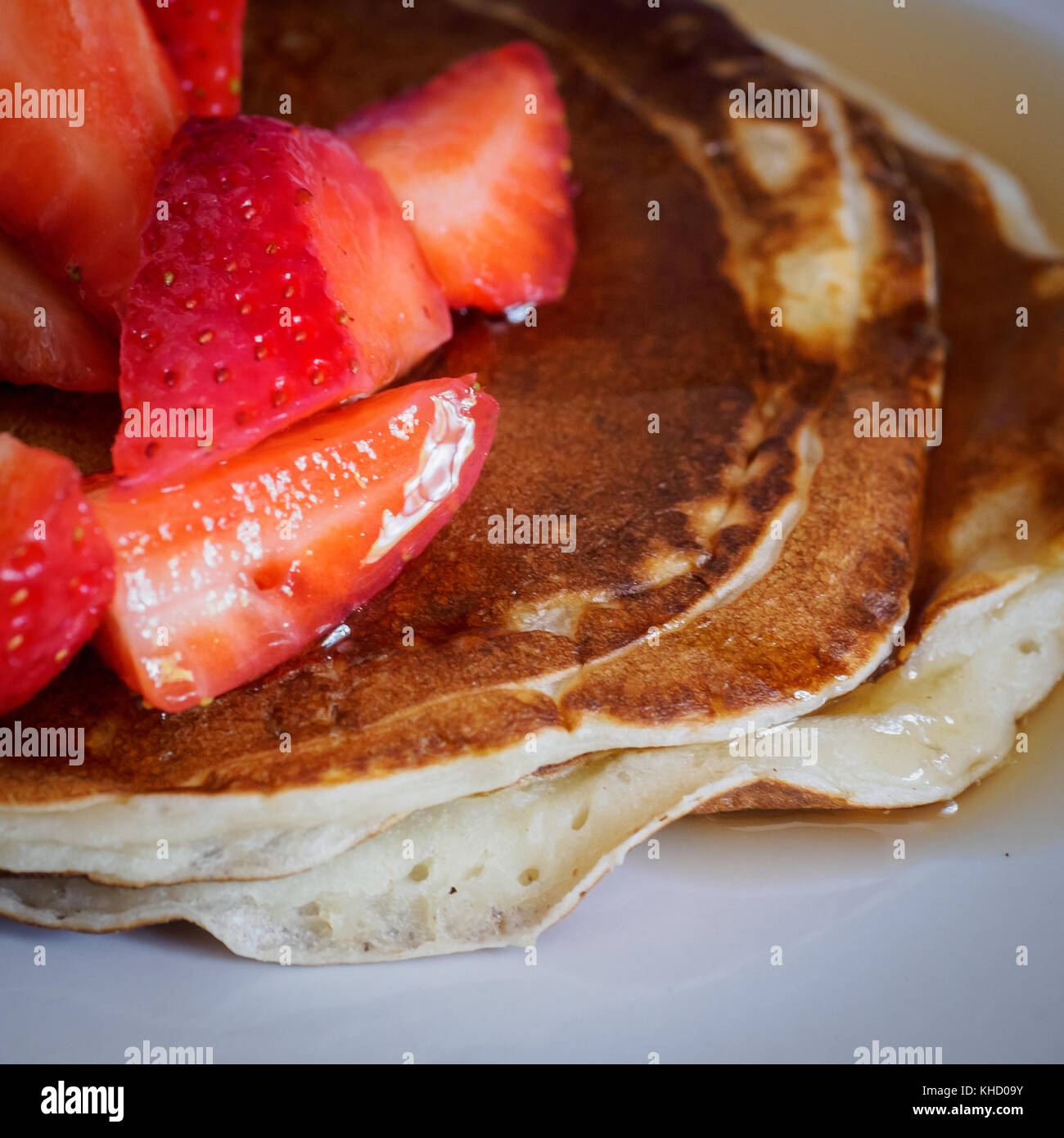 Cerca de una pila de panqueques caseros en una placa blanca con cortar las fresas y el jarabe de arce en la parte superior. Formato cuadrado. Foto de stock