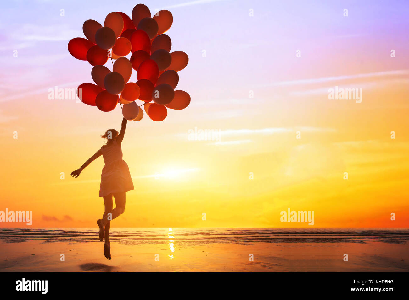 La felicidad o el concepto de ensueño, silueta de mujer feliz saltando con globos multicolores al atardecer en la playa Foto de stock
