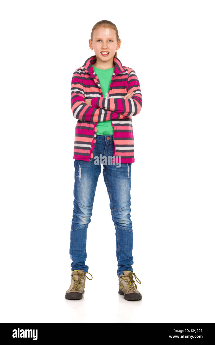 Sonriente joven rubia en rayas Chaqueta polar, pantalones vaqueros y botas  de trekking de pie con los brazos cruzados y mirando a la cámara. longitud  completa studio shot es Fotografía de stock -