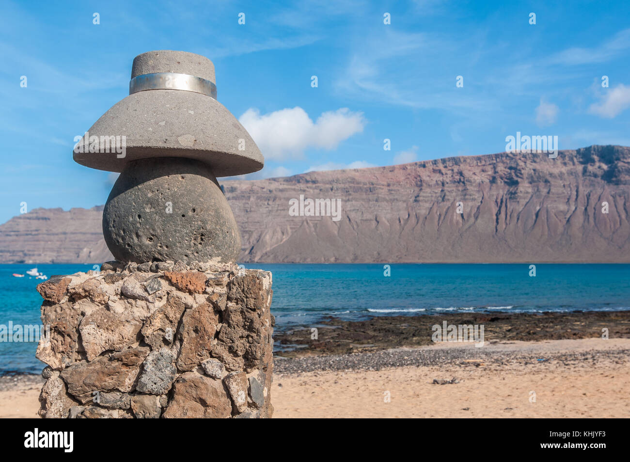 Vista de una calle típica con una estatua de piedra de un típico sombrero  en primer plano y la playa, en el fondo, La Graciosa, Islas Canarias,  España Fotografía de stock -