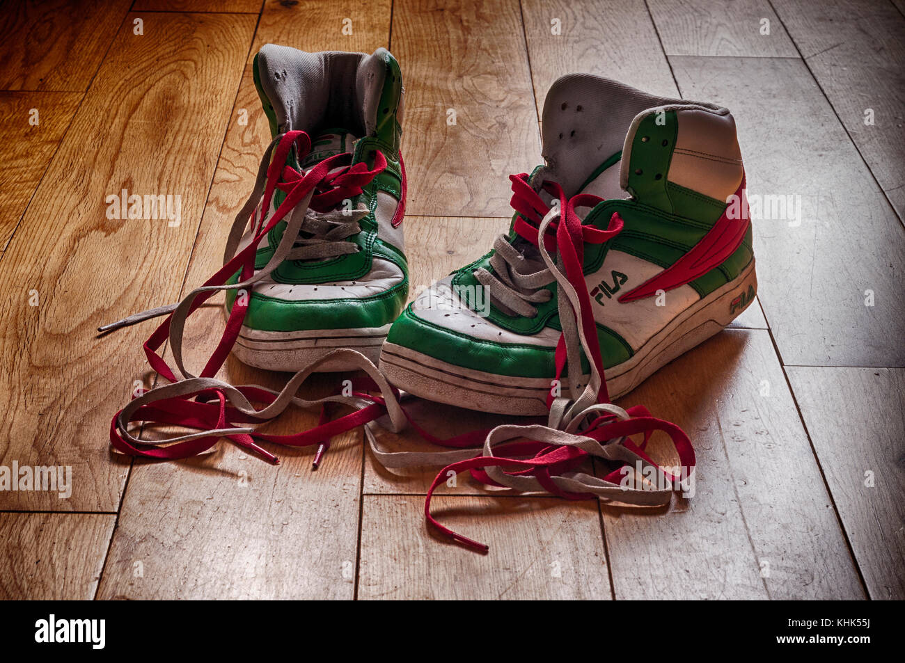 Botas fila (zapatillas) que han sido usadas y comienzan a mostrar su edad con cordones de colores. Sentado en un suelo de madera Fotografía de stock - Alamy