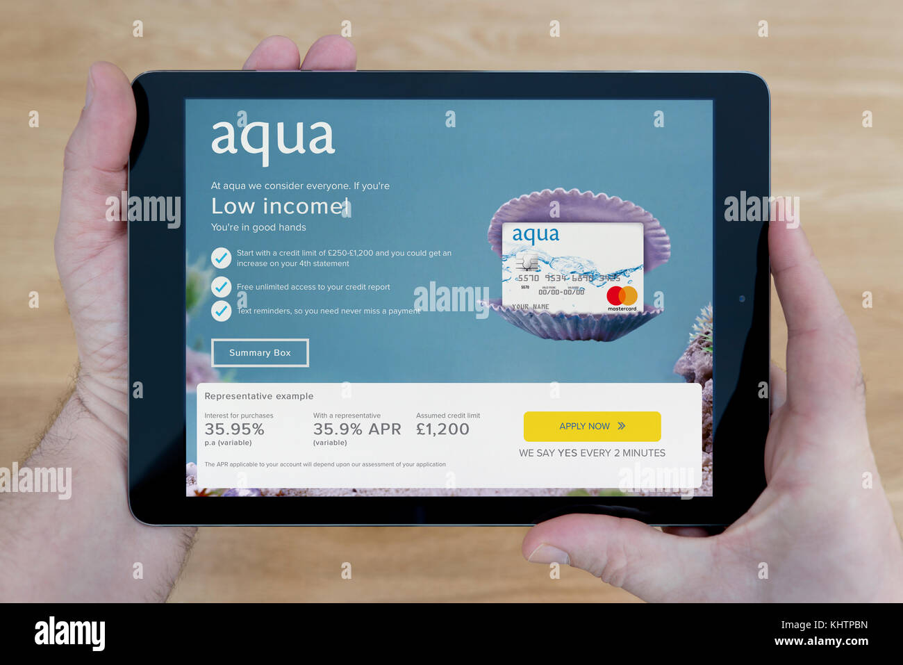 Un hombre se ve en el sitio web de tarjeta de Aqua en su iPad dispositivo tablet, disparó contra una mesa de madera fondo superior (uso Editorial solamente) Foto de stock