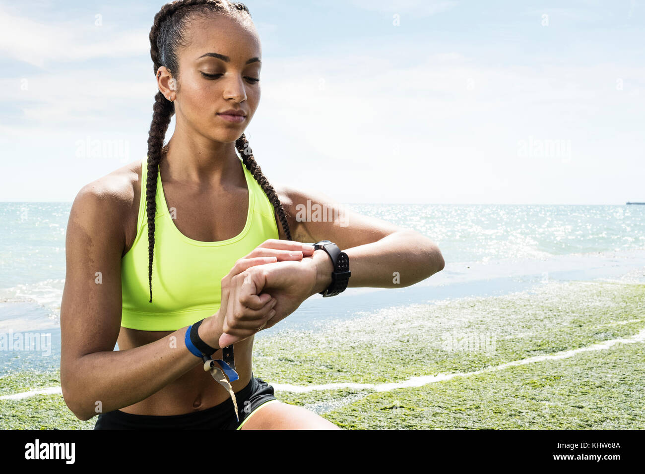 Mujer joven junto al mar, vistiendo ropa deportiva, mirando el rastreador de actividades Foto de stock