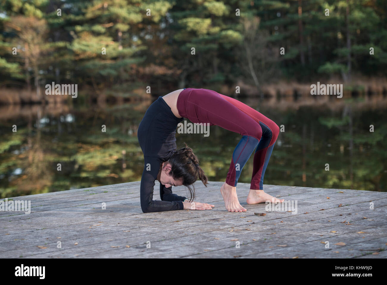 Mujer practicando yoga por un lago haciendo un puente pose. Foto de stock