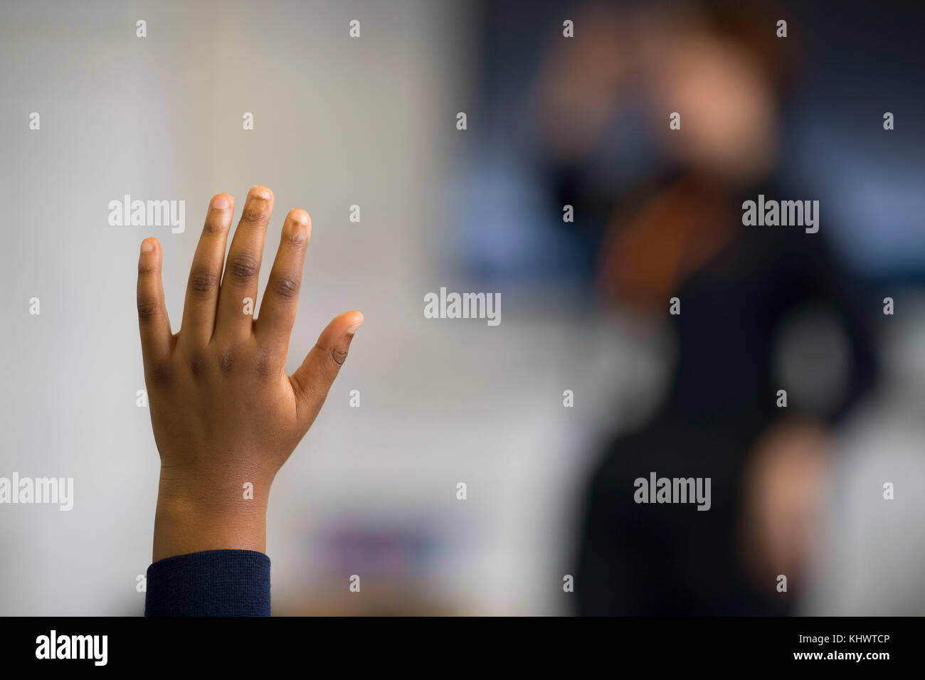Un joven niño negro pone su mano hacia arriba cuando hace una pregunta en un aula en Gales, Reino Unido. Foto de stock