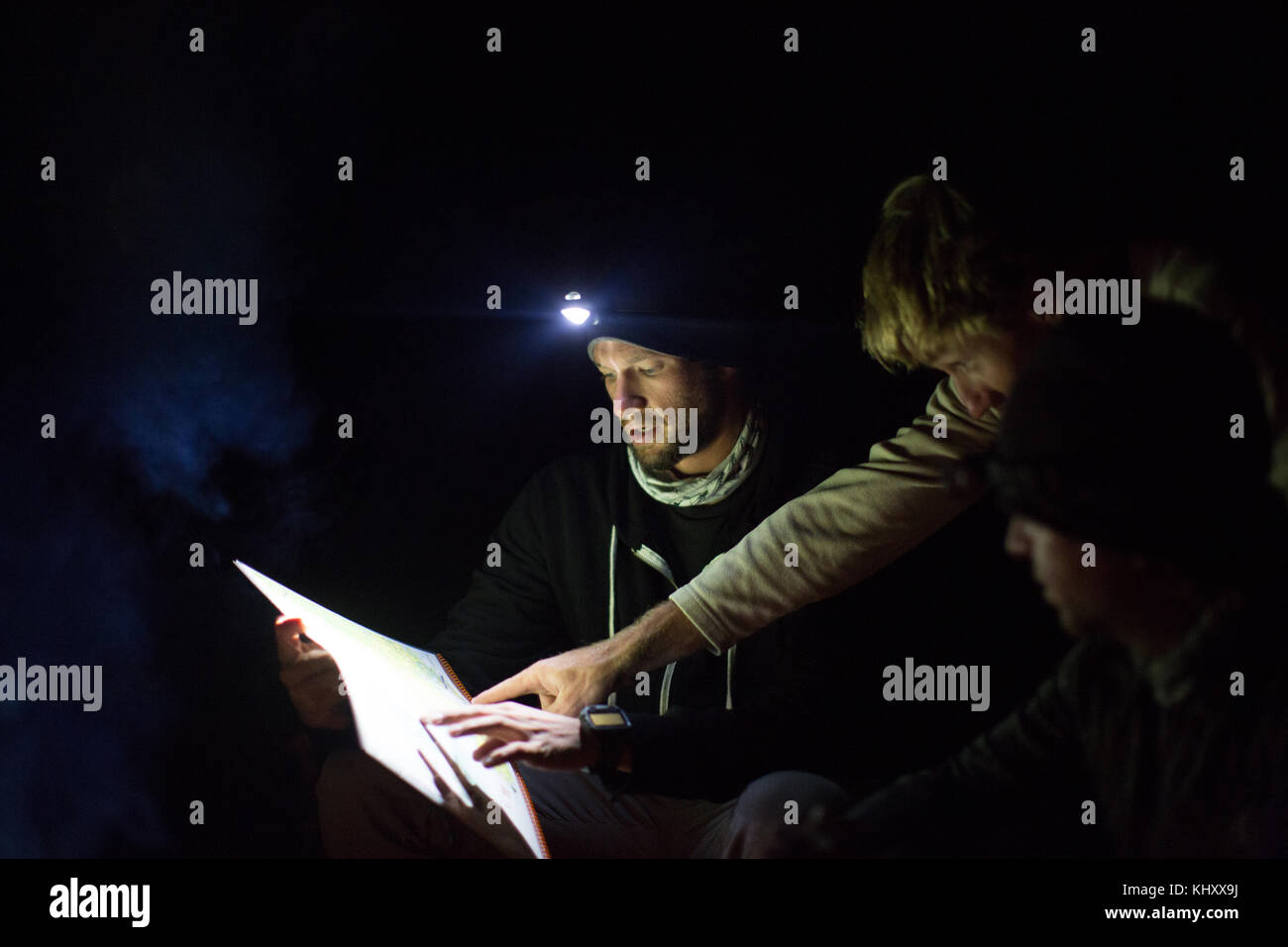 Tres hombres que buscan en el mapa, en la noche, con la luz de faro Foto de stock