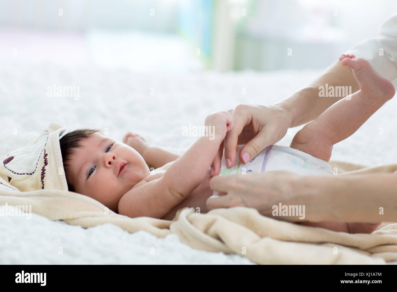 Madre poniendo en su pañal bebé feliz en vivero Foto de stock