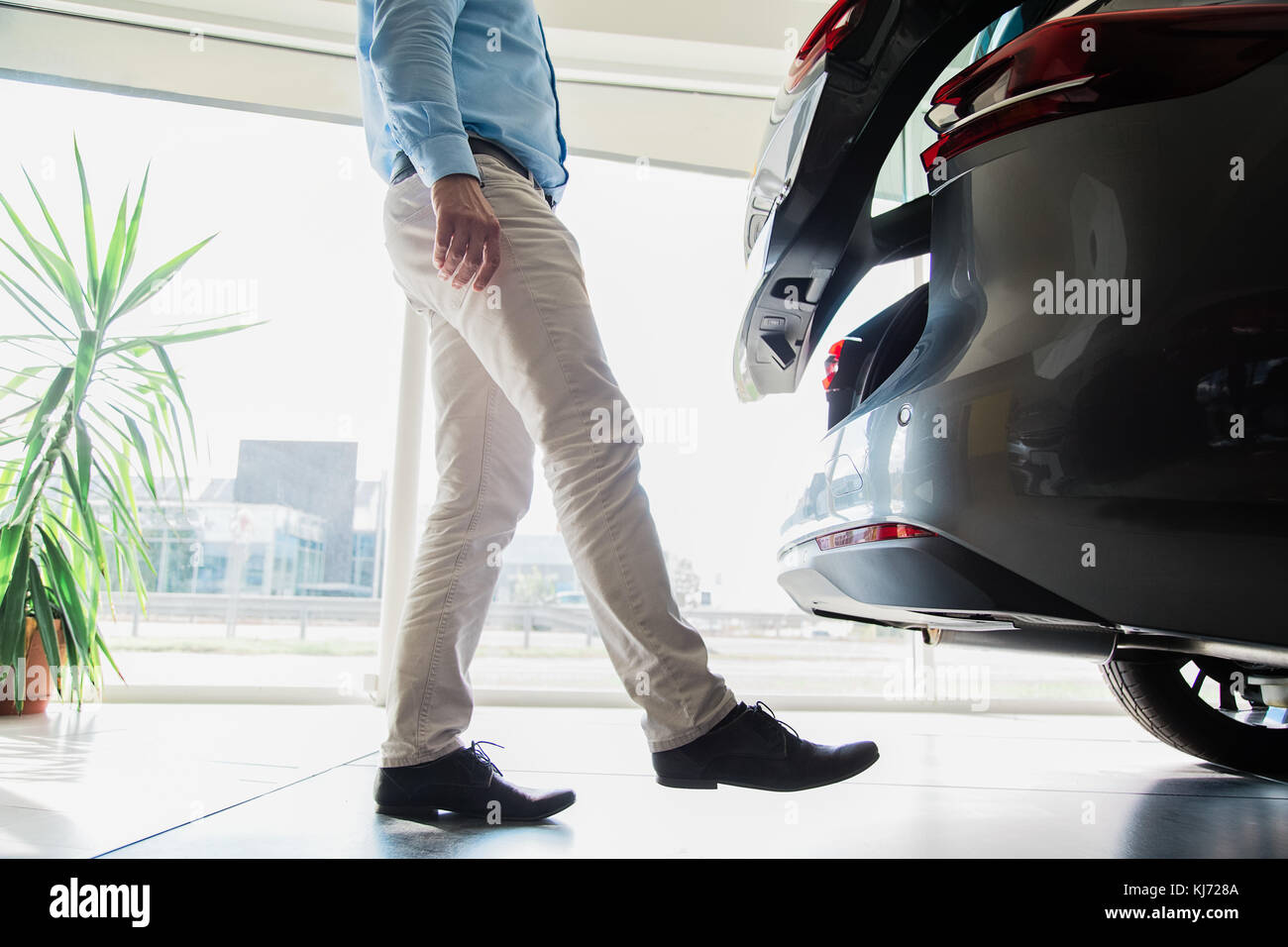 Cerca del macho adulto piernas abriendo la puerta de un automóvil con el movimiento de las piernas, sin tener que utilizar la llave del auto, tomadas en interiores en el concesionario de coches Foto de stock
