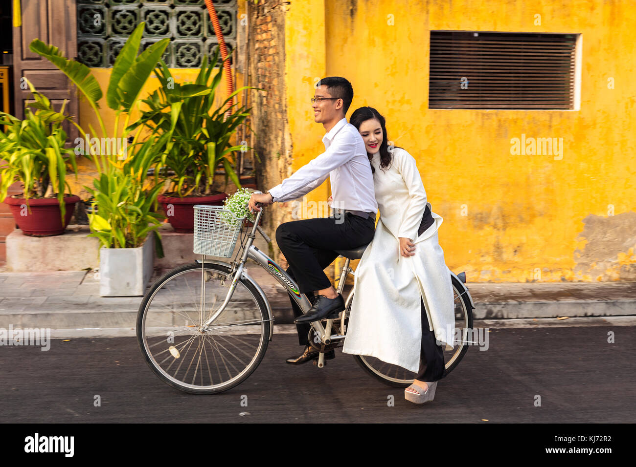 Joven recién casado Pareja en bicicleta en el centro de historia de Hoi An, Vietnam, Asia, declarado Patrimonio de la Humanidad por la Unesco Foto de stock