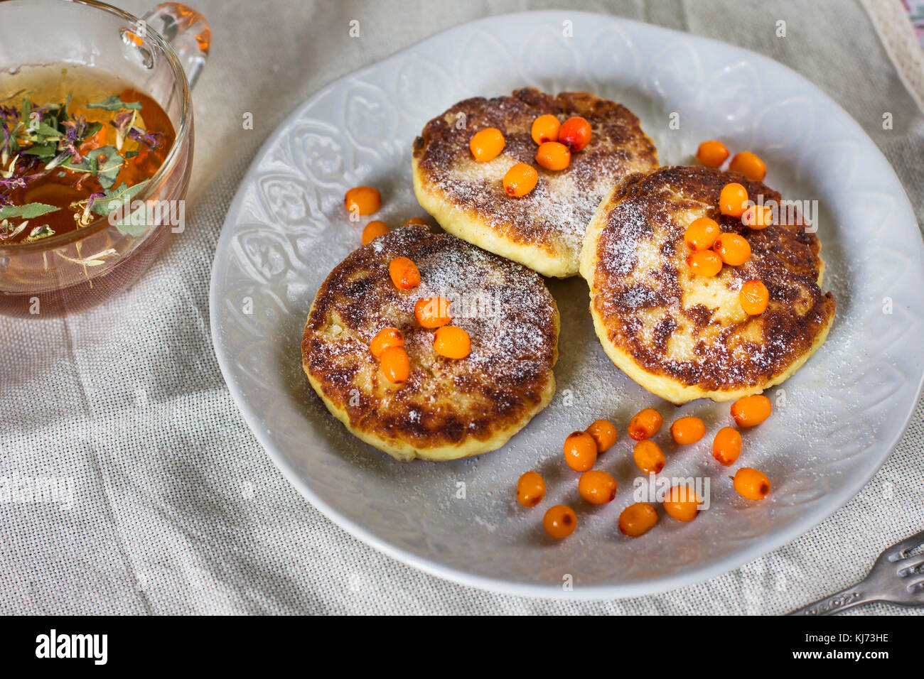 El queso cottage panqueques con bayas de espino cerval de mar y té de hierbas. Desayuno saludable Foto de stock