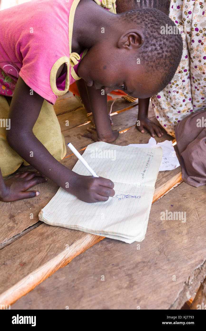 Joven ugandesa escribir y dibujar en un libro de ejercicios en la sombra de un puesto en el mercado sin usar, Uganda, África Foto de stock