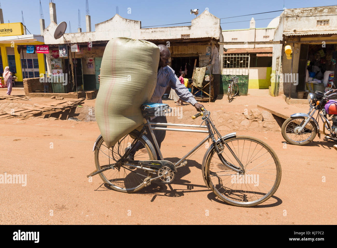 .Ugandés transportar bicicletas hombre caminando con un gran saco en el asiento de la bicicleta, Uganda, África Oriental Foto de stock