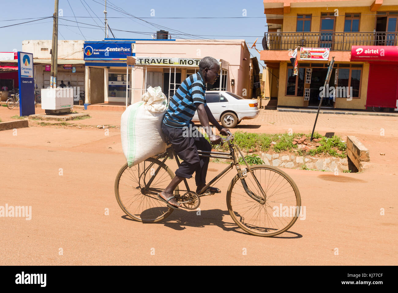 Un hombre de Uganda el ciclismo en una bicicleta con una bolsa grande en la espalda, Uganda, África Oriental Foto de stock