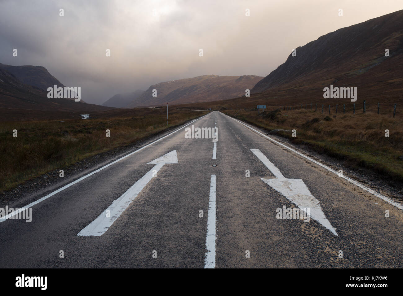 A82 a través de Glencoe, Escocia, Reino Unido, con las flechas de dirección en la carretera en invierno al amanecer Foto de stock