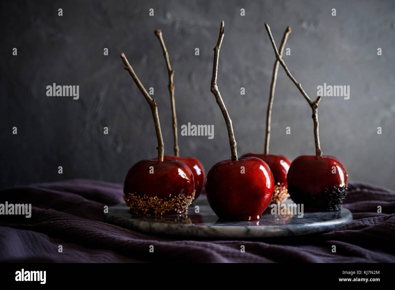 Bandeja de mármol precioso, rojo, manzanas de caramelo en lino de color púrpura oscuro. Moody sentir con oscuro fondo de textura. Foto de stock
