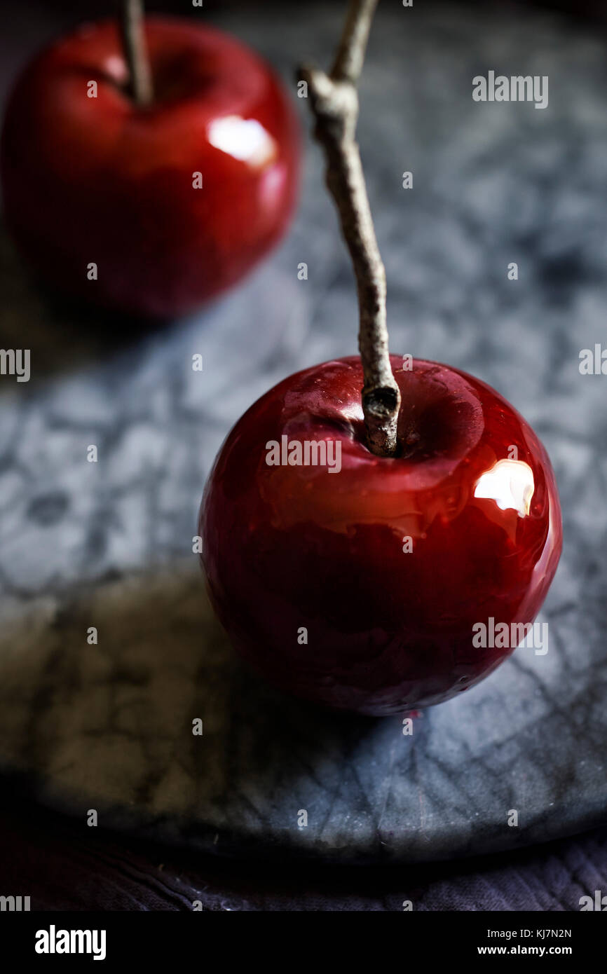 Detalle de la filmación, rojo brillante manzana de caramelo con twig stick en una bandeja de mármol oscuro, Moody sentir. Foto de stock