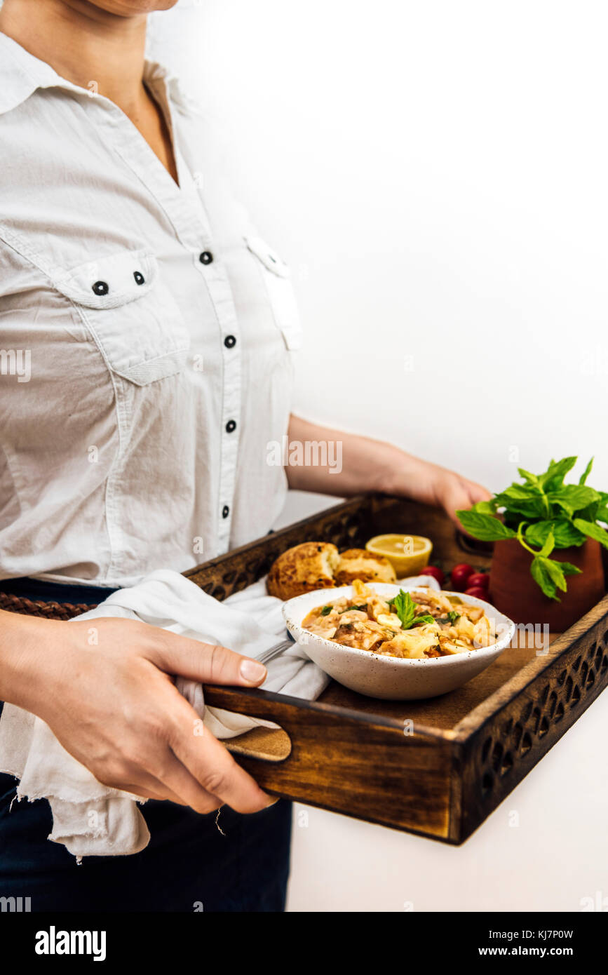 Una mujer con una camisa blanca sosteniendo una bandeja con un tazón de sopa de col, Diner Rollos, hojas de menta fresca fotografiadas desde la vista frontal. Foto de stock