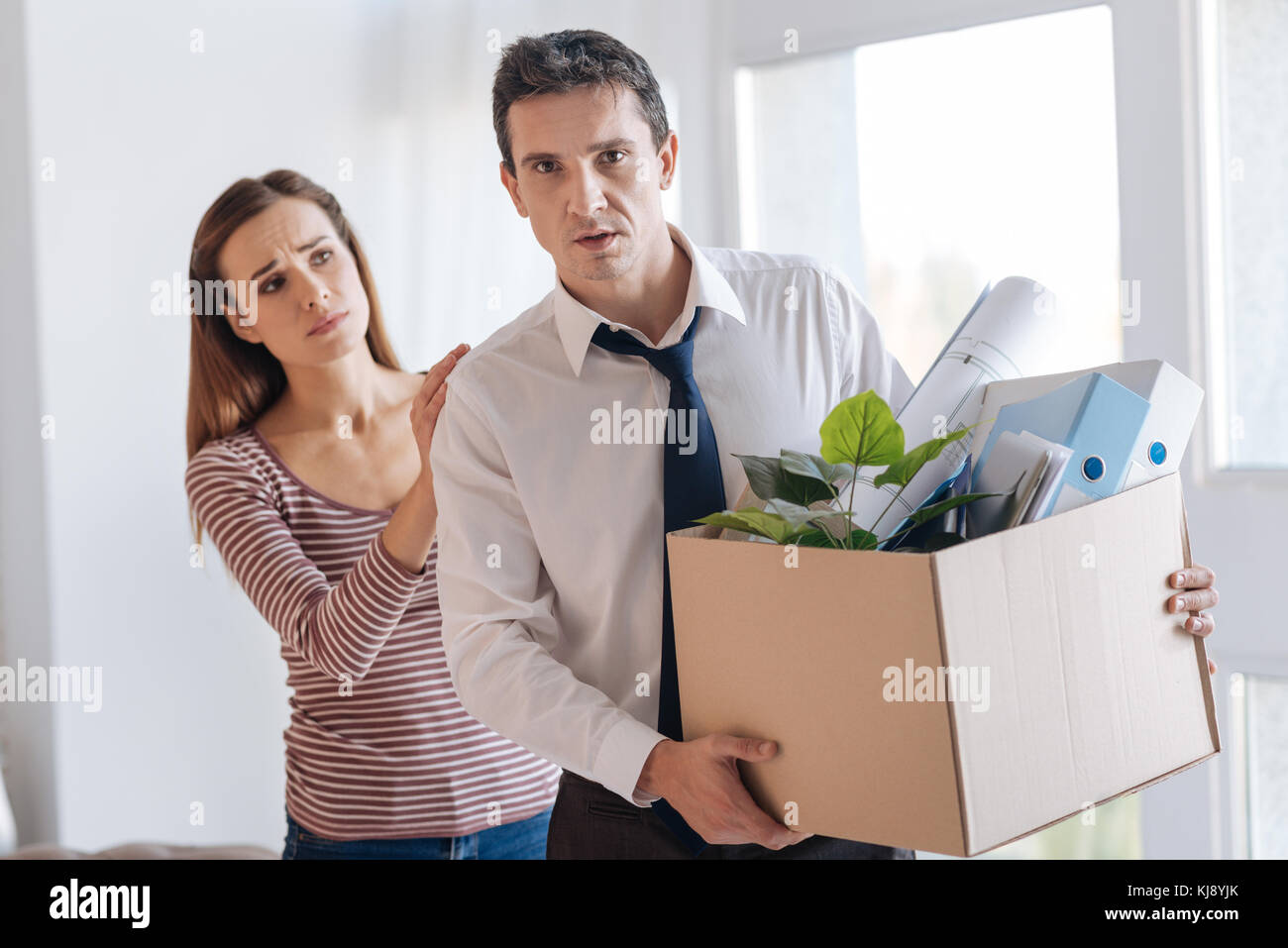 Destituido el hombre lleva una caja pesada mientras su esposa le reconfortante Foto de stock