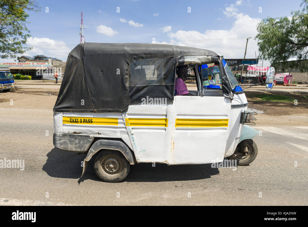 Un blanco de tres ruedas manejando taxis tuk tuk en la carretera a través de una pequeña ciudad, Kenia, África Oriental Foto de stock