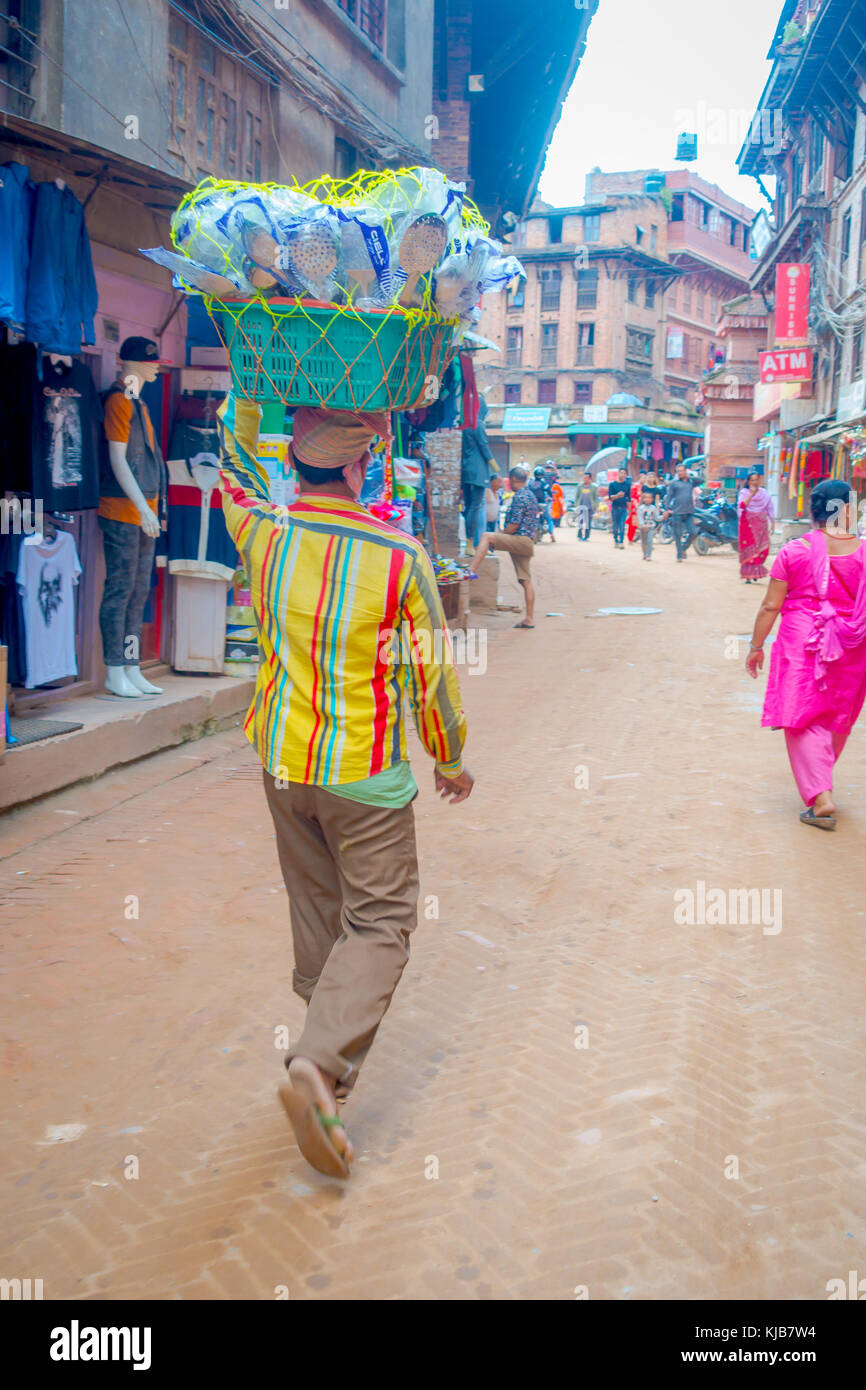 Bhaktapur, Nepal - Noviembre 04, 2017: hombre no identificado llevando sobre su cabeza una cesta con cucharas en el exterior del edificio antiguo cerca de los mercados, con turistas paseando en Bhaktapur, Nepal Foto de stock