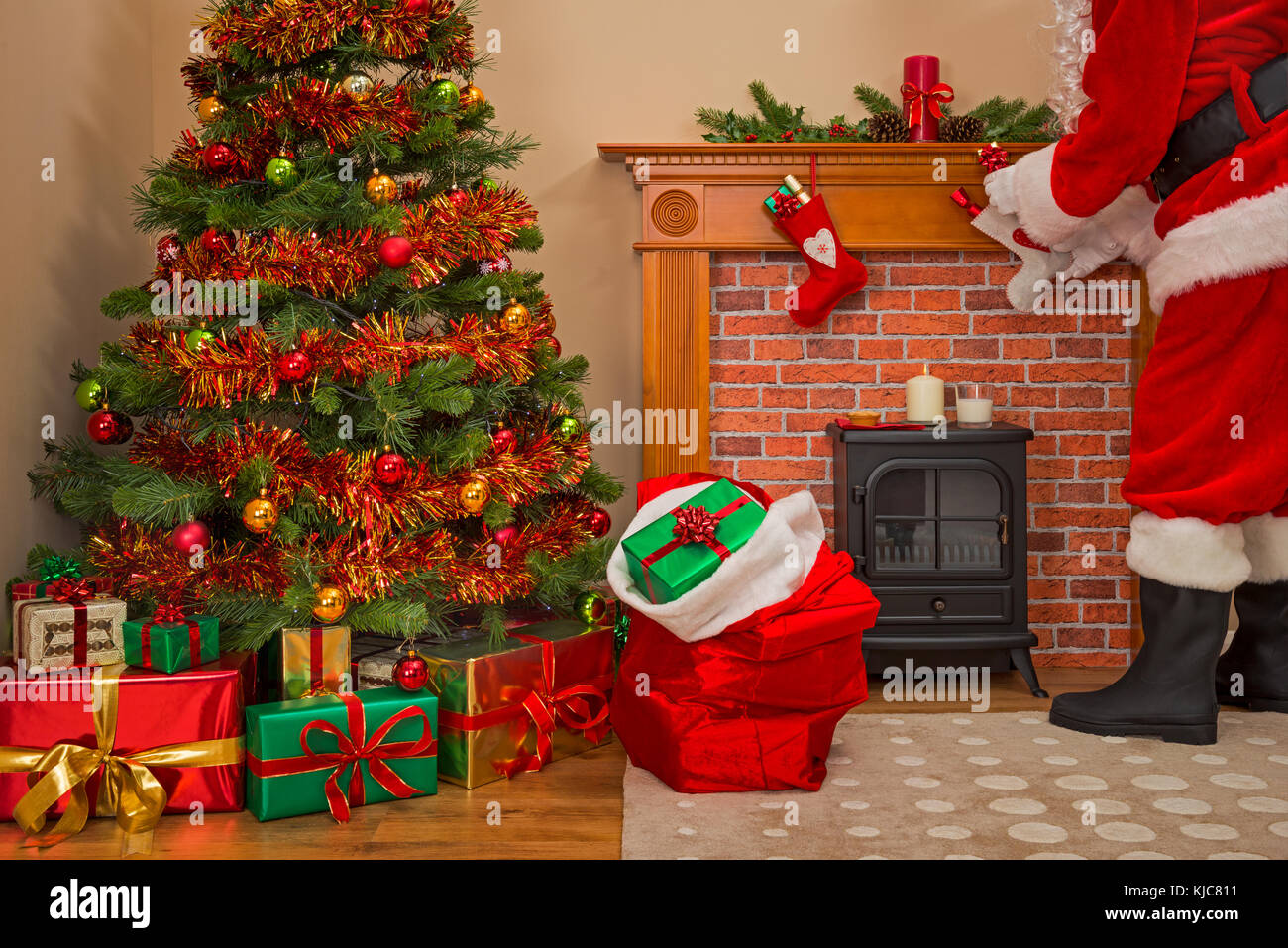Santa Claus entregando regalos regalos envueltos bajo el árbol de navidad con un saco lleno de juguetes para niños y niñas buenas. Foto de stock