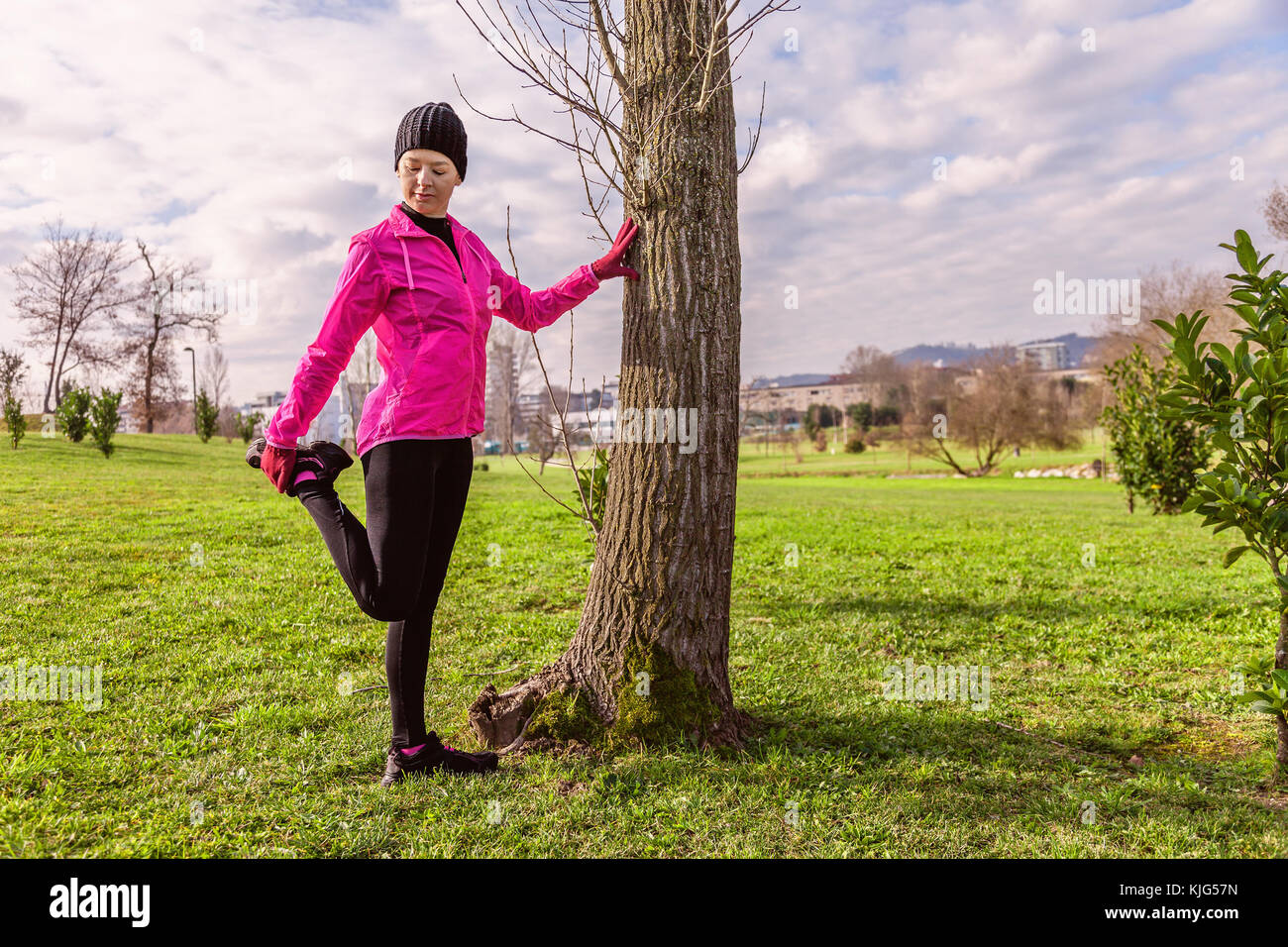 Mujer joven calentar y estirar las piernas antes de ejecutar en un frío invierno, otoño de día de otoño en un parque urbano. atleta femenina vistiendo windb rosa Foto de stock