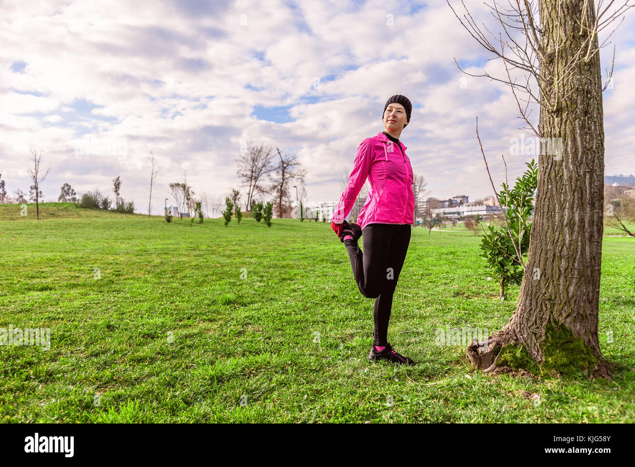 Mujer joven calentar y estirar las piernas antes de ejecutar en un frío invierno, otoño de día de otoño en un parque urbano. atleta femenina vistiendo windb rosa Foto de stock