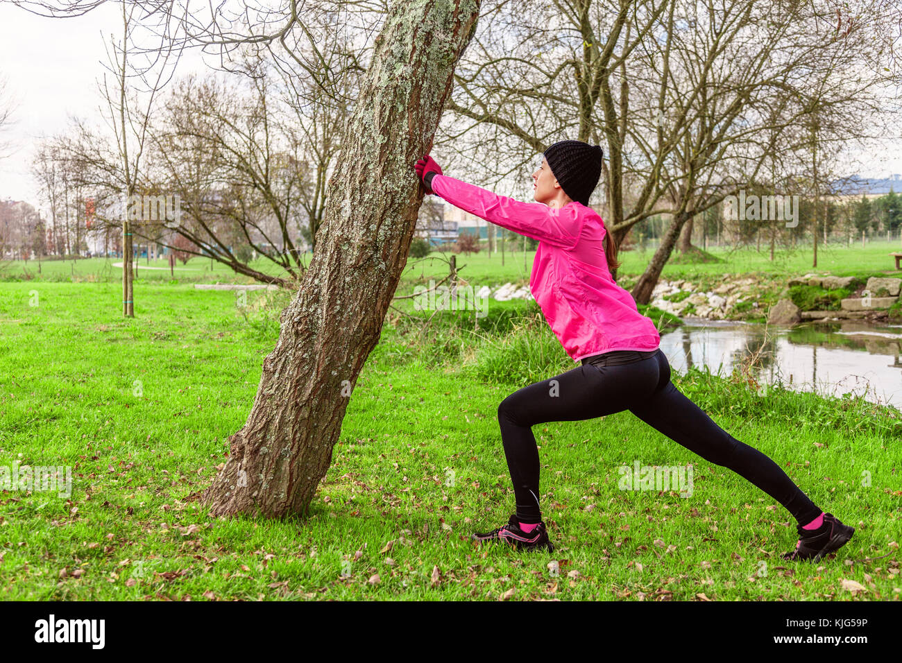 Mujer joven calentar y estirar las piernas antes de ejecutar en un frío invierno, otoño de día de otoño en un parque urbano. atleta femenina vistiendo windb rosa Foto de stock