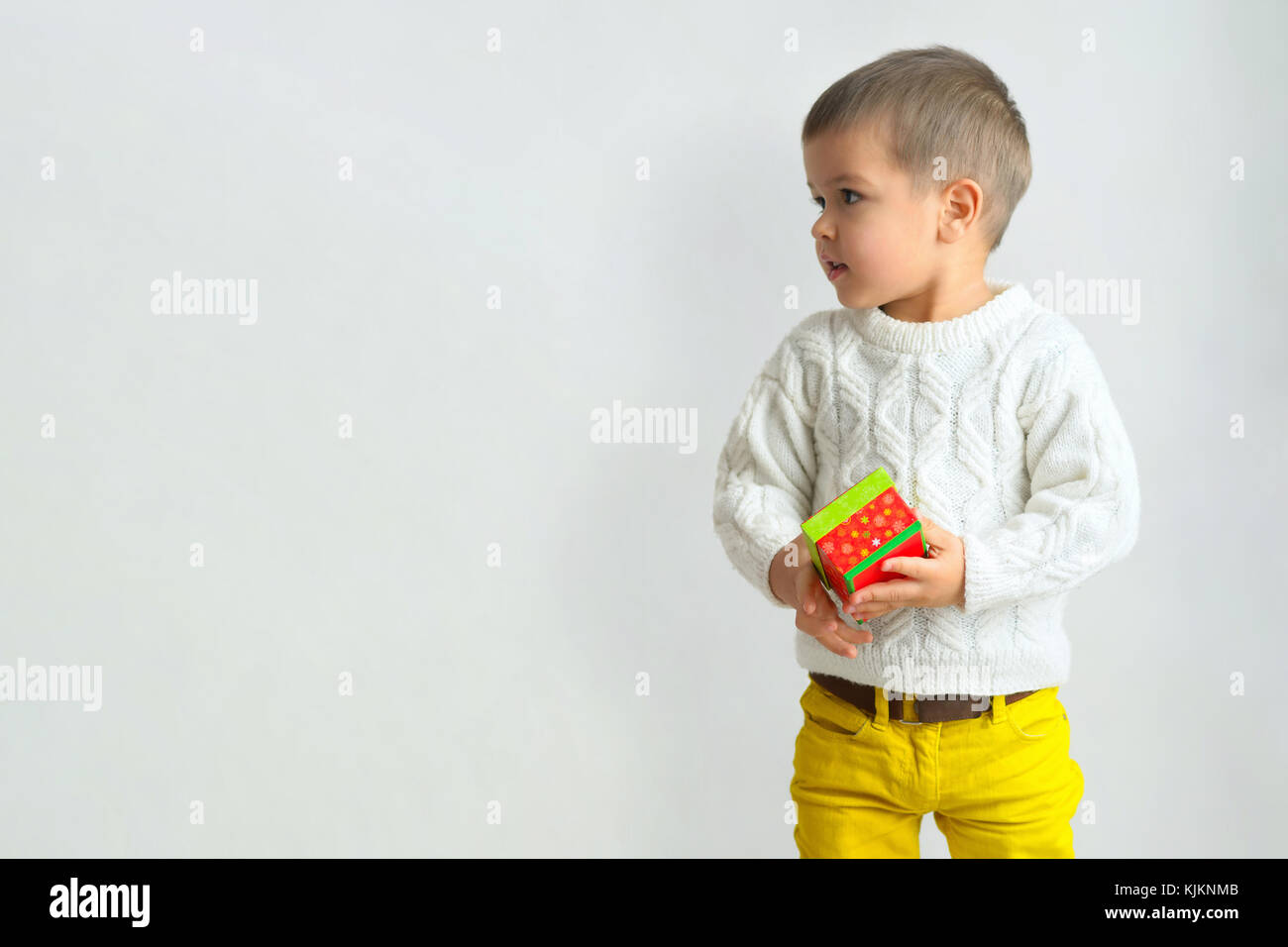 Niño en un suéter blanco y pantalón amarillo es la celebración de un regalo  de año nuevo cuadro. aislado sobre fondo Fotografía de stock - Alamy