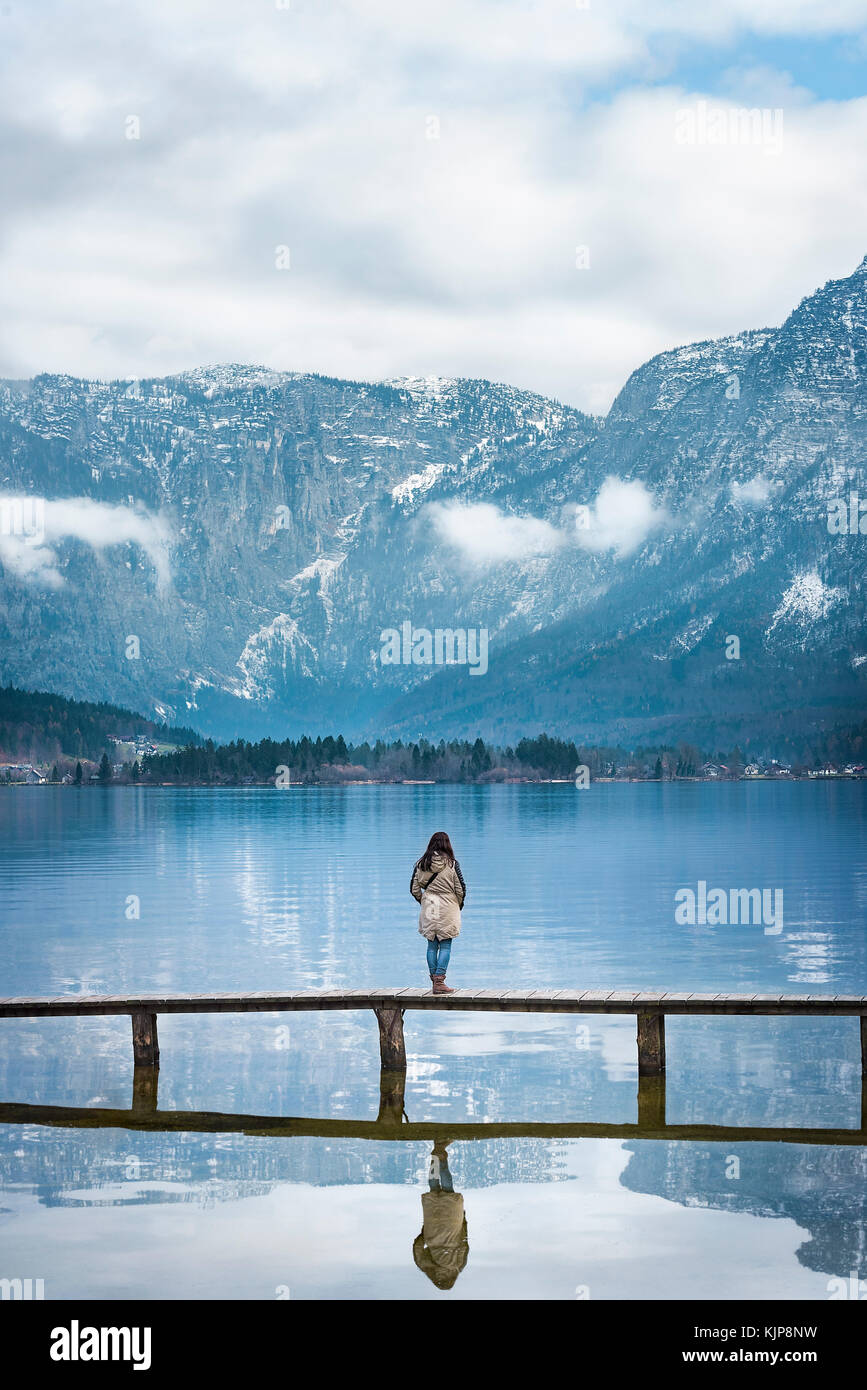 Lugares famosos tema imagen con una mujer de pie en la cubierta, mirando a los Alpes austriacos y el lago hallstatter, ubicado en Hallstatt, Austria Foto de stock