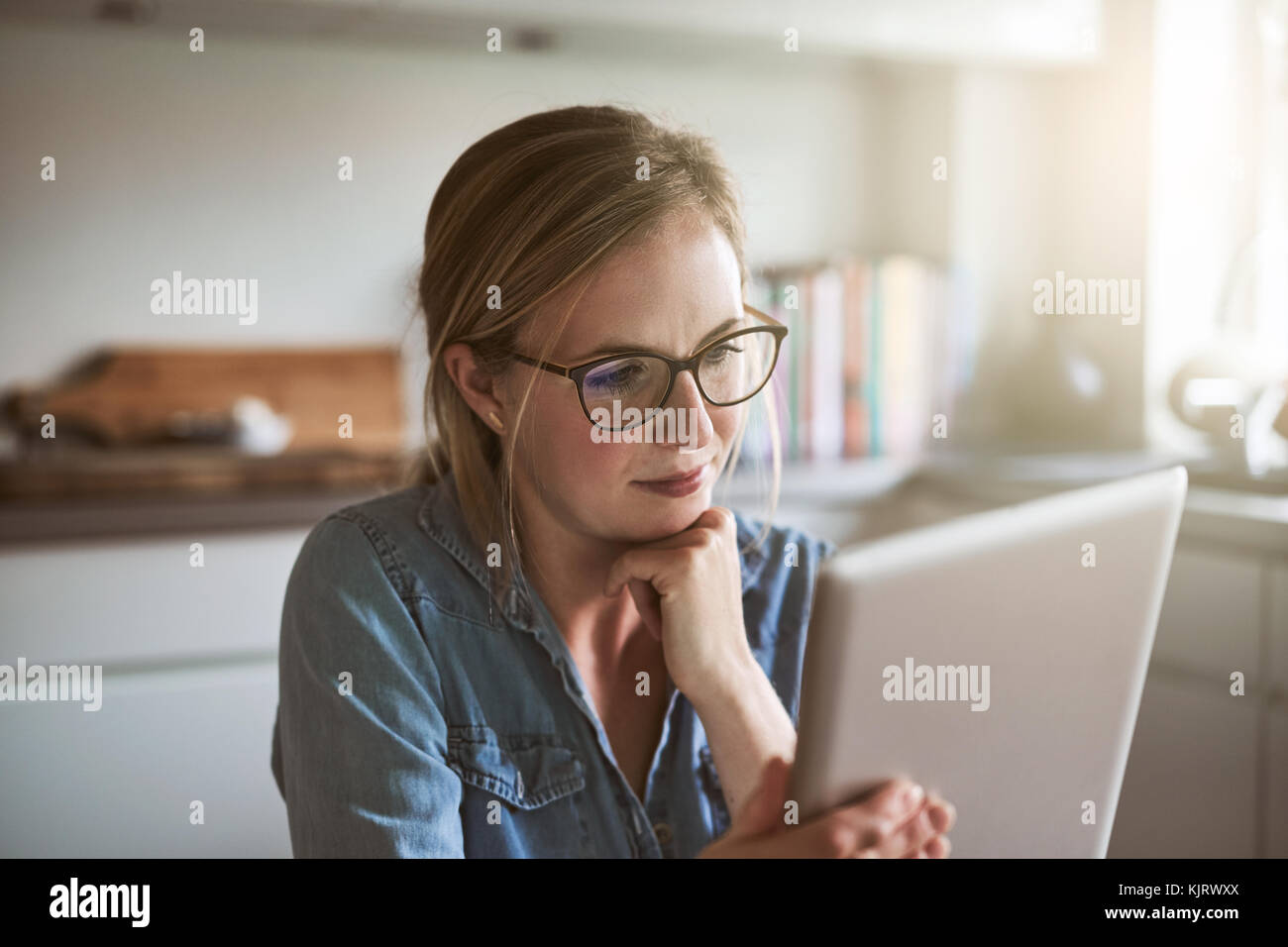 Joven empresario trabajando en su pequeña empresa con una tableta digital mientras está sentada sola en la mesa de su cocina en casa Foto de stock