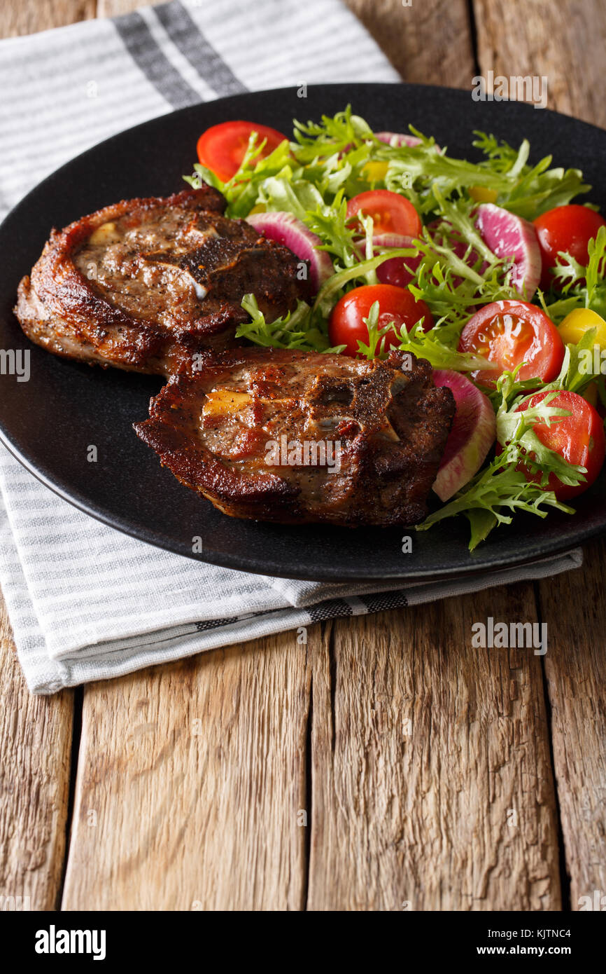 Delicioso filete de cordero y ensalada de verduras de rábanos, tomates y lechuga cerca en una placa vertical. Foto de stock