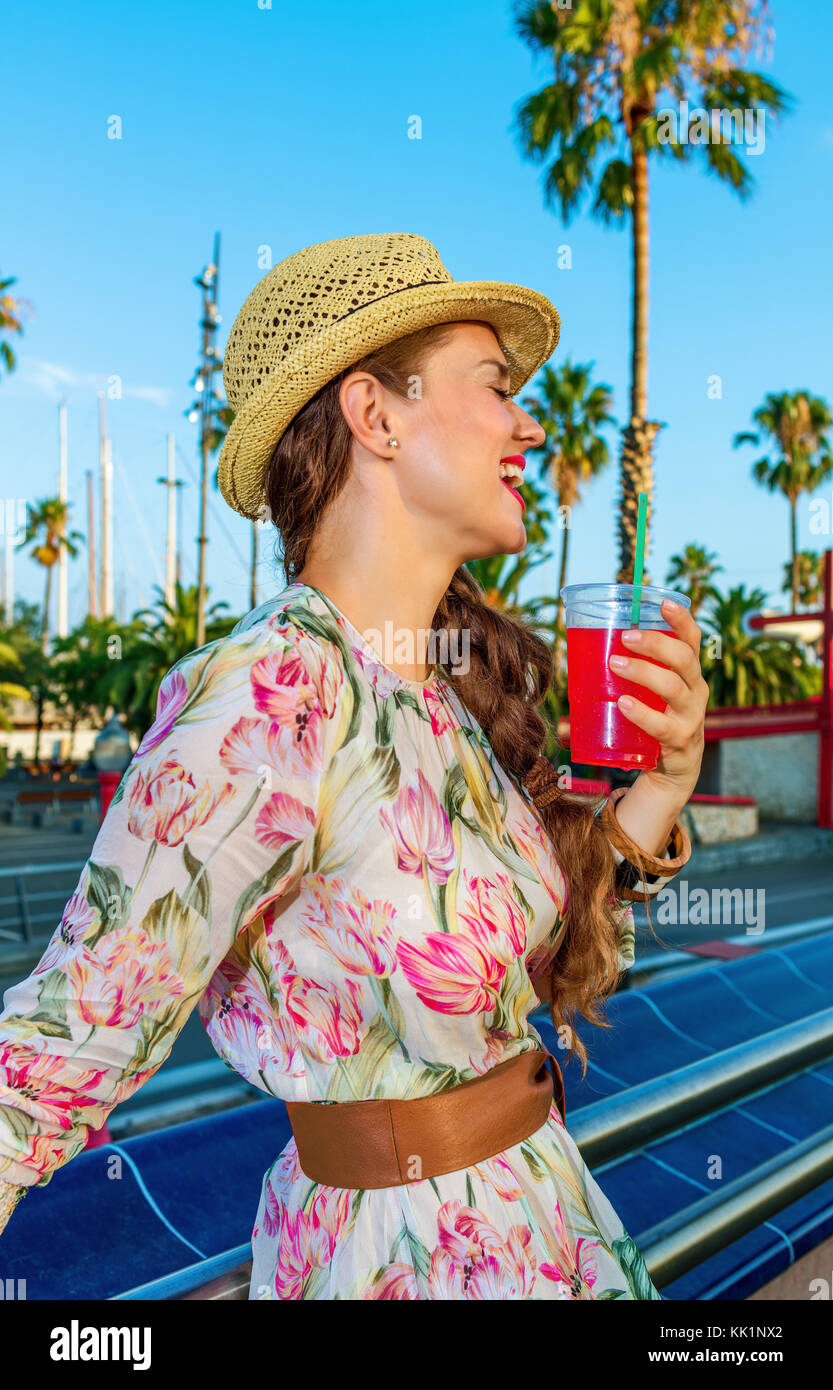 En verano colorido barcelona. Feliz turista elegante mujer en vestido largo  y sombrero de paja sobre el terraplén en Barcelona, España, con bebidas de  color rojo brillante r Fotografía de stock -