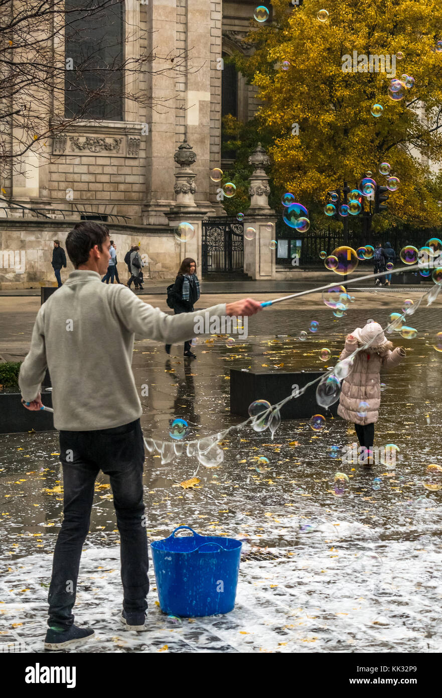 Hombre en St Pauls Cathedral entretenido a un niño con grandes burbujas, Londres, Inglaterra, Reino Unido. Foto de stock