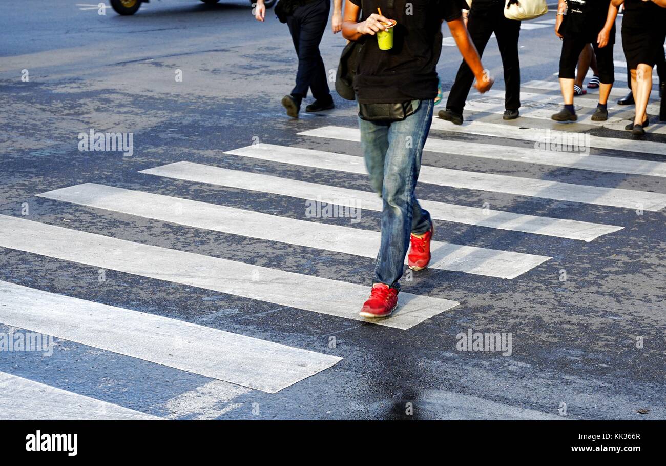 Hombre vestido con pantalones de mezclilla y zapatos rojos sosteniendo un  vaso de té verde de cruzar la calle, cruce peatonal con multitud de gente  durante las horas pico, Bangkok, Tailandia Fotografía