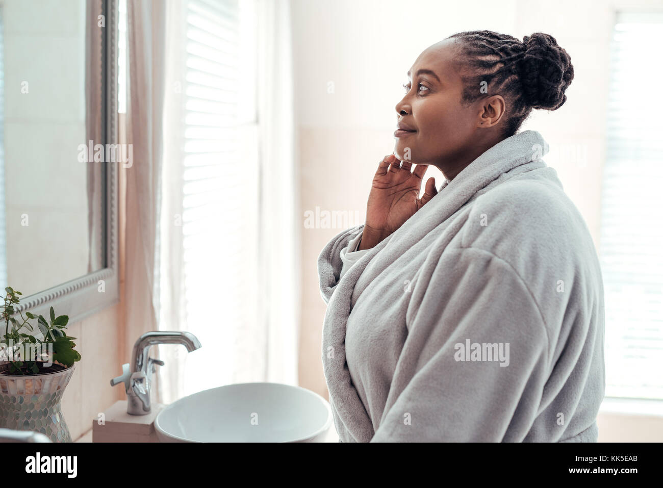 Mujer africana mirando su cutis en un espejo del baño Foto de stock