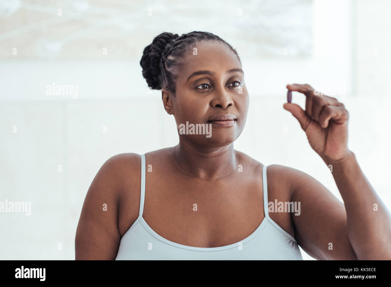 Ansiosa mujer africana mirando una píldora en su mano Foto de stock