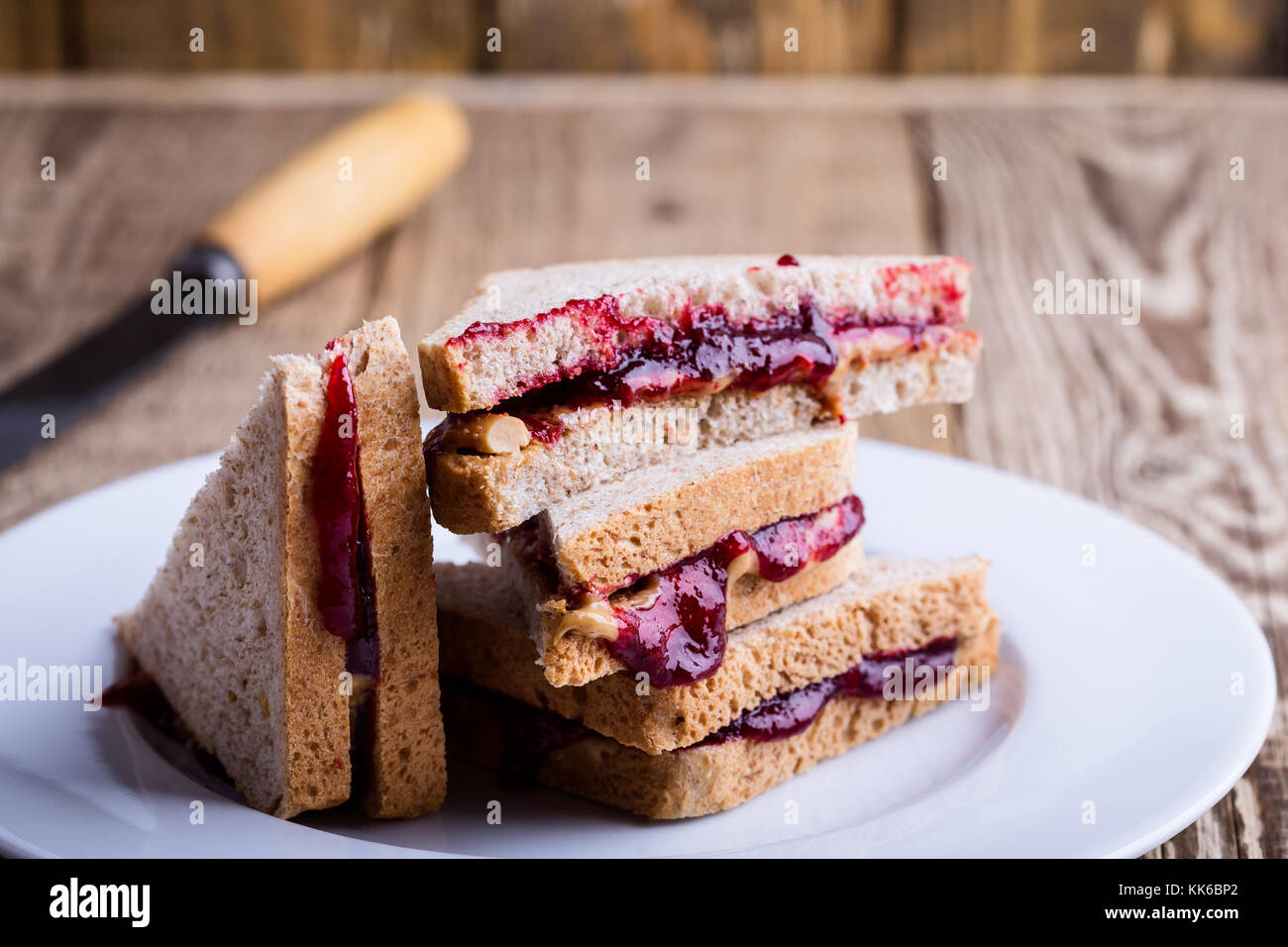 Sándwich de mantequilla de maní y mermelada con pan de trigo entero sobre mesa de madera rústica Foto de stock