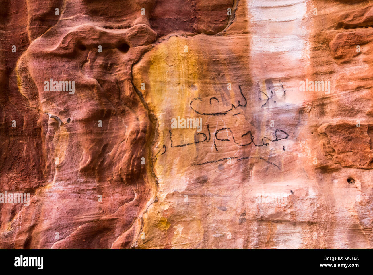 Cerca de arenisca rosada y naranja patrones de mineral en el acantilado, Petra, Jordania, Oriente Medio, con el Árabe graffiti Foto de stock
