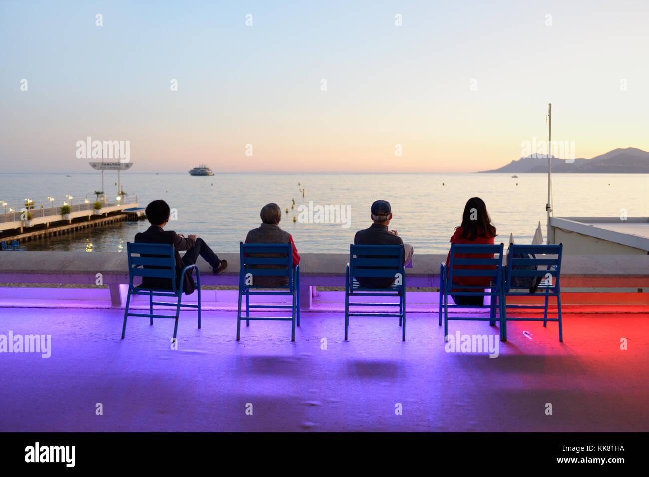 Cuatro turistas disfrutan de la puesta de sol en el Boulevard de la Croisette, Cannes, en Dusk, con la espectacular iluminación de la calle Color, Riviera Francesa, francia Foto de stock