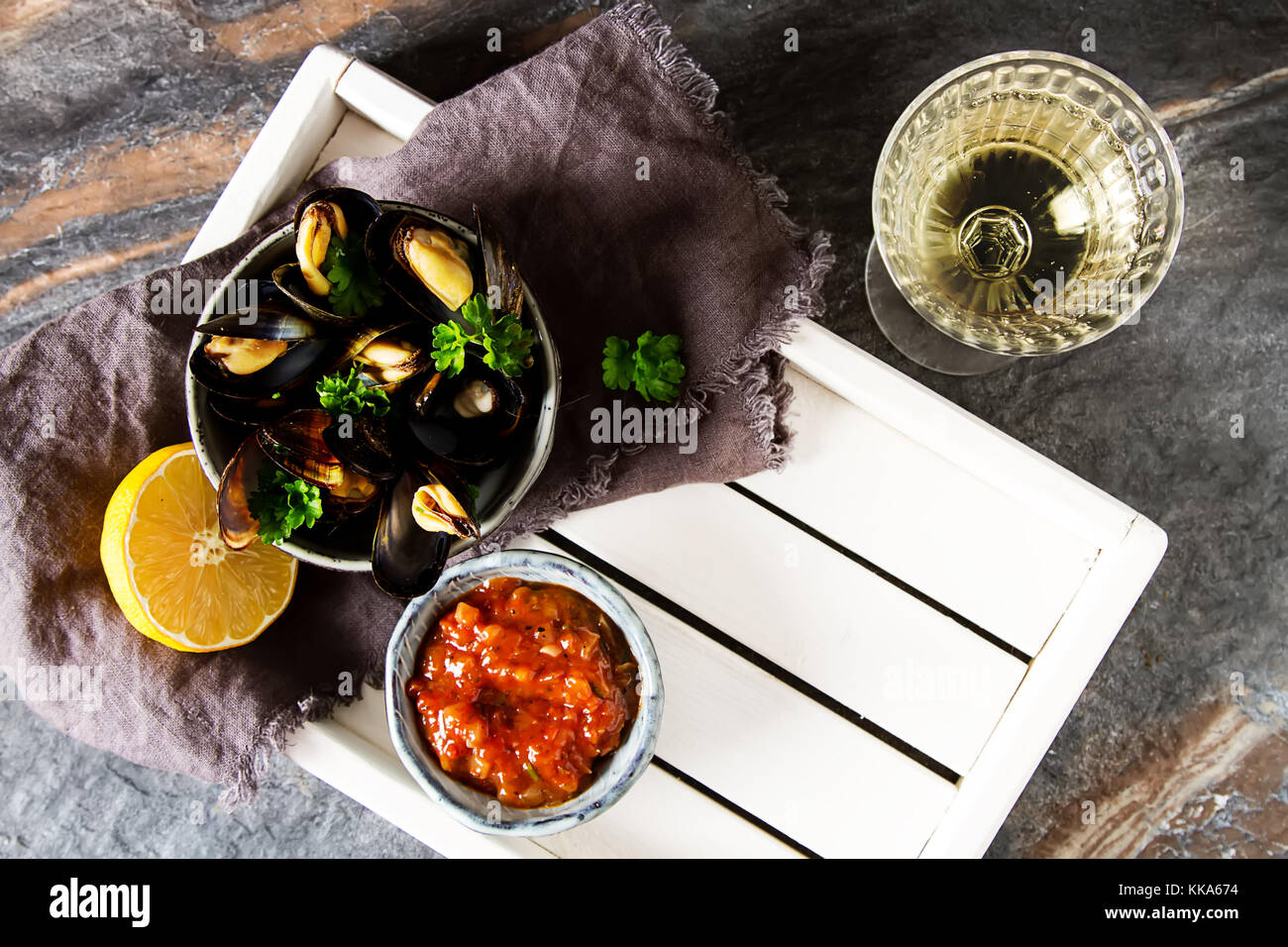 Mejillones con hierbas en un tazón con limón y vino blanco sobre una tabla de madera.. la comida de mariscos a la orilla del mar francés. fondo oscuro Foto de stock