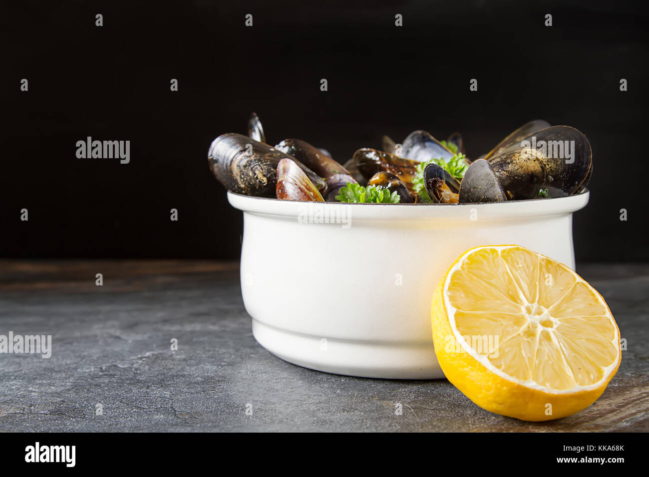 Mejillones con hierbas en un recipiente blanco con limón. mariscos. Comida en la orilla del mar francés. fondo oscuro Foto de stock