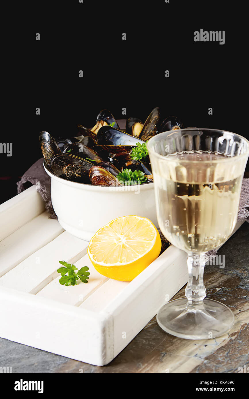 Mejillones con hierbas en un tazón con limón y vino blanco sobre una tabla de madera.. la comida de mariscos a la orilla del mar francés. fondo oscuro Foto de stock