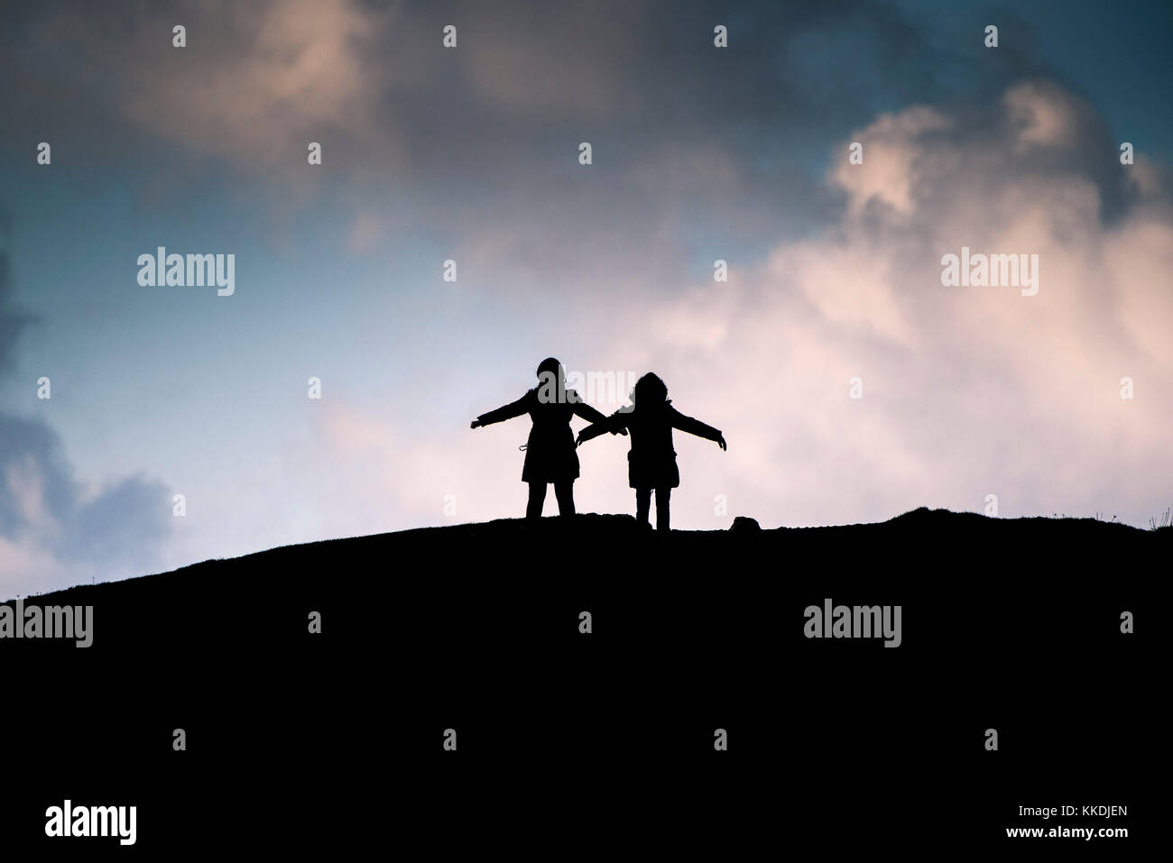 Siluetas - la silueta de dos personas de pie con sus brazos estirados en vientos fuertes en la cumbre de East Panire Newquay Cornwall Reino Unido. Foto de stock