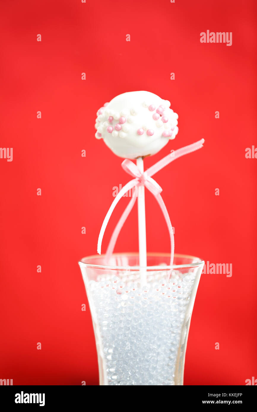 Una sola cakepop sobre fondo rojo. Foto de stock