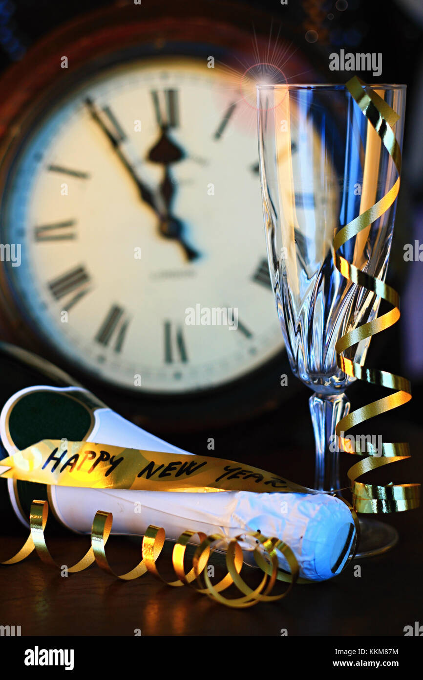 Reloj de año nuevo en el fondo con el vaso vacío y streamers también una botella de champán pone sobre la mesa Foto de stock